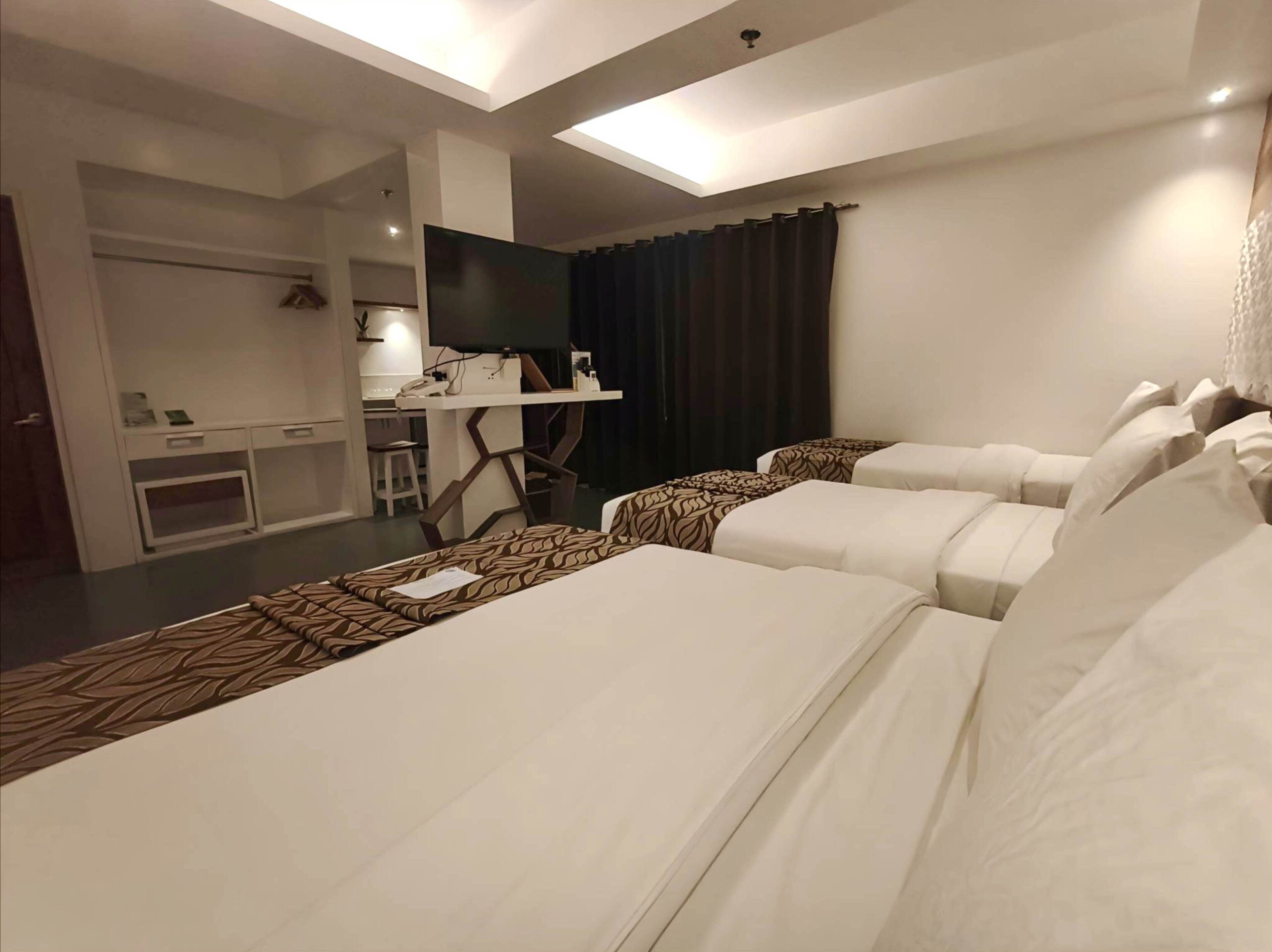 Ein Hotelzimmer mit zwei Betten, einem Schreibtisch, einem Fernseher und einer kleinen Küchenzeile.