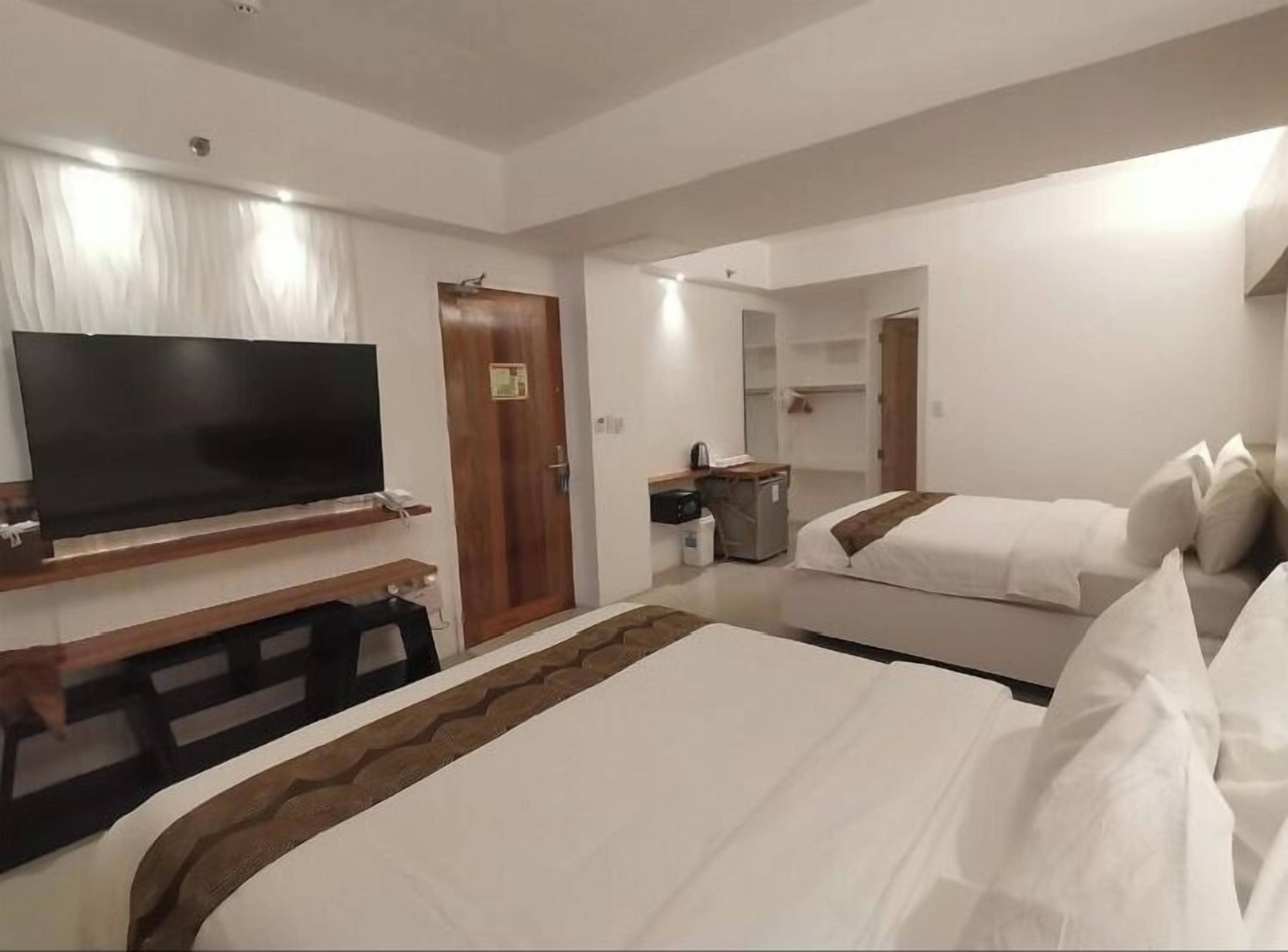 A hotel room with a large bed, a TV on a wooden stand, a desk with a chair, a wardrobe, and a bathroom with a mirror and sink.