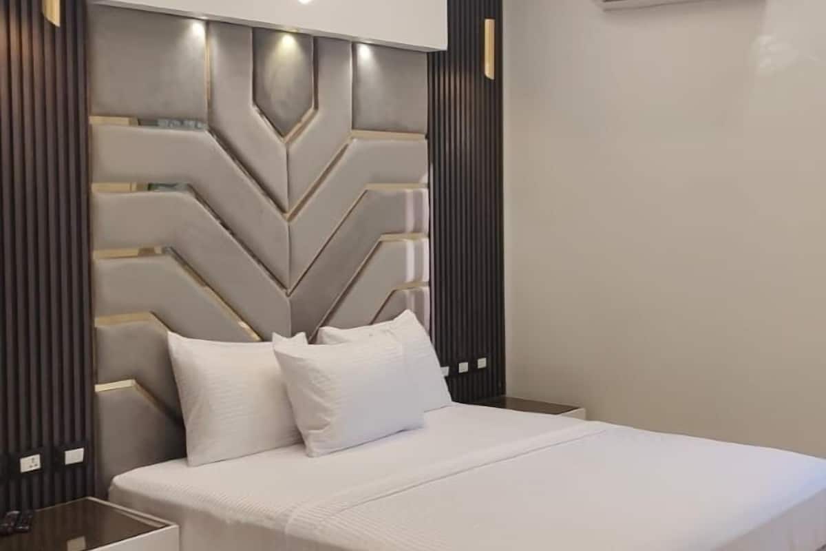 A modern bedroom with a geometric headboard, a bedside table, and an air conditioning unit.