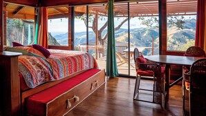 A wooden cabin with a bed, a dining table, and a view of the mountains. - El Sol Monteverde (Monteverde)