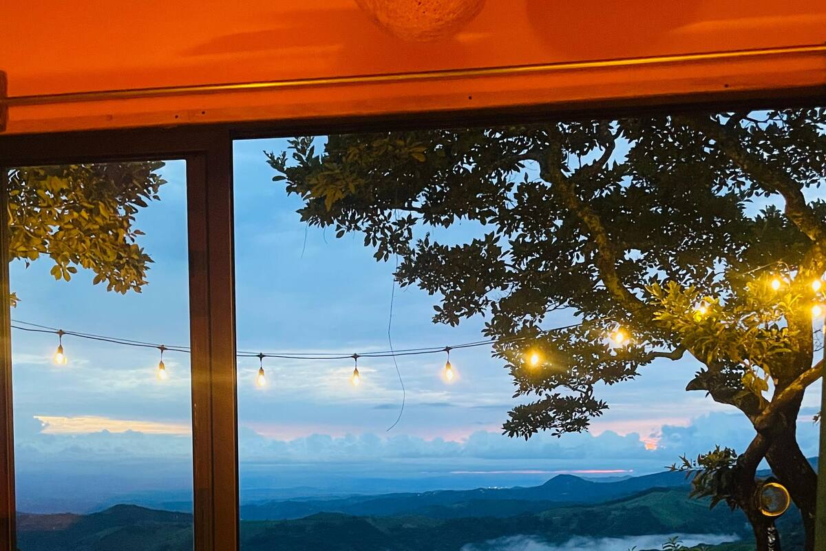 A room with a bed, a table, and a view of a mountainous landscape.