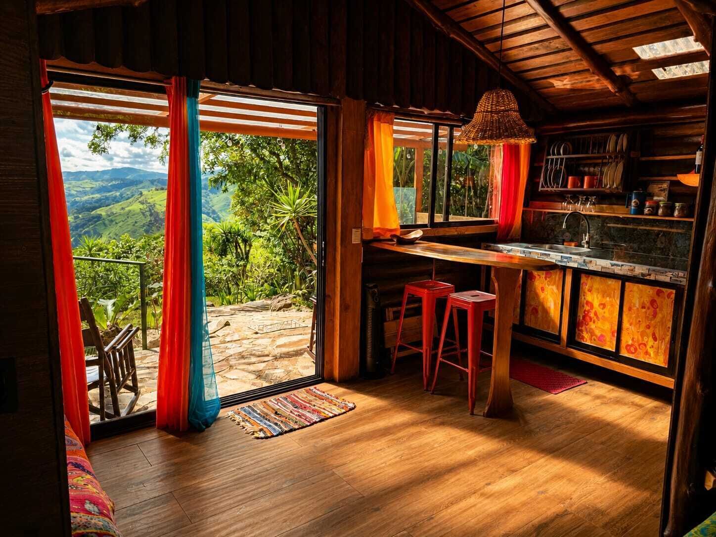 A wooden interior with a kitchen area, bar, and large windows overlooking a mountainous landscape.
