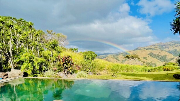 A clear pool with a stone border, surrounded by lush greenery and a view of distant hills. - El Sol Monteverde (Monteverde)