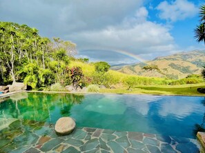 A clear pool with a stone border, surrounded by lush greenery and a view of distant hills. - El Sol Monteverde (Monteverde)