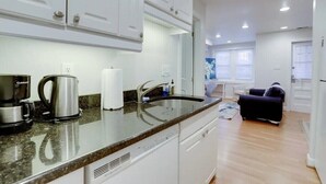 Una cocina moderna con armarios blancos, encimera de granito, cafetera y lavamanos.