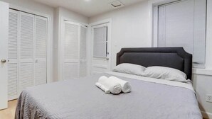 Un dormitorio con una cama, armarios blancos y una ventana con persianas.