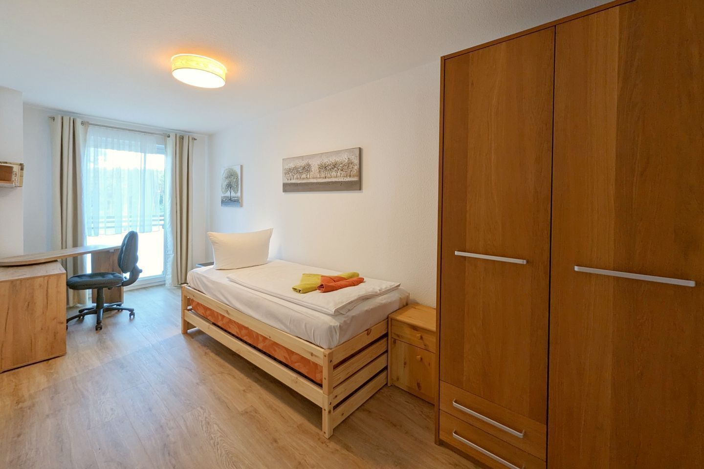 A bedroom with a bed, a desk, a chair, and a wardrobe.