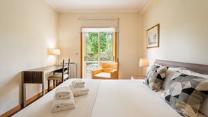 A hotel room with a bed, two bedside lamps, a chair, a desk, and a window with a view of greenery. - GuestReady - A paradisíac stay in Fão (Esposende)