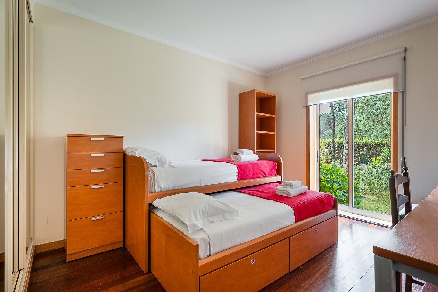 Une chambre avec un lit superposé, une commode en bois et une porte-fenêtre coulissante donnant sur un jardin.