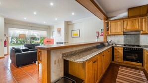 A modern kitchen with wooden cabinets, a granite countertop, and a built-in oven. - GuestReady - A paradisíac stay in Fão (Esposende)