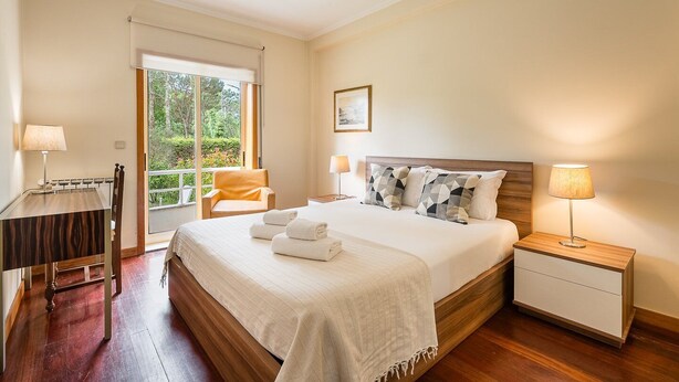 A hotel room with a large bed, a desk, a chair, and a nightstand with lamps. - GuestReady - A paradisíac stay in Fão (Esposende)