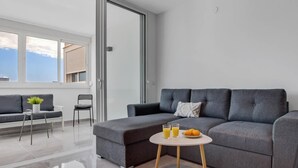 A modern living room with a grey sofa, a small round table with drinks and fruit, and a chair. - Micarlo 701 - Second line of beach. 2 bedrooms (Torremolinos)