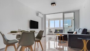 A modern living room with a dining area, large windows, and a flat-screen TV. - Micarlo 701 - Second line of beach. 2 bedrooms (Torremolinos)