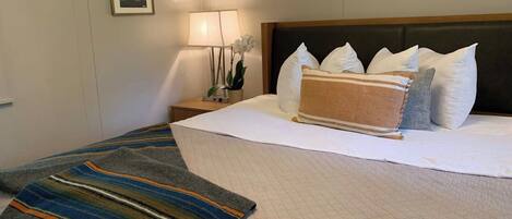 A hotel room with a bed, pillows, a bedside lamp, a nightstand, and a framed picture on the wall.