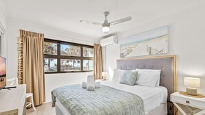 A neatly arranged bedroom with a bed, a desk, a chair, a bedside table, and a ceiling fan. - Spinnaker Apt 6- Mooloolaba Beach  (Mooloolaba)