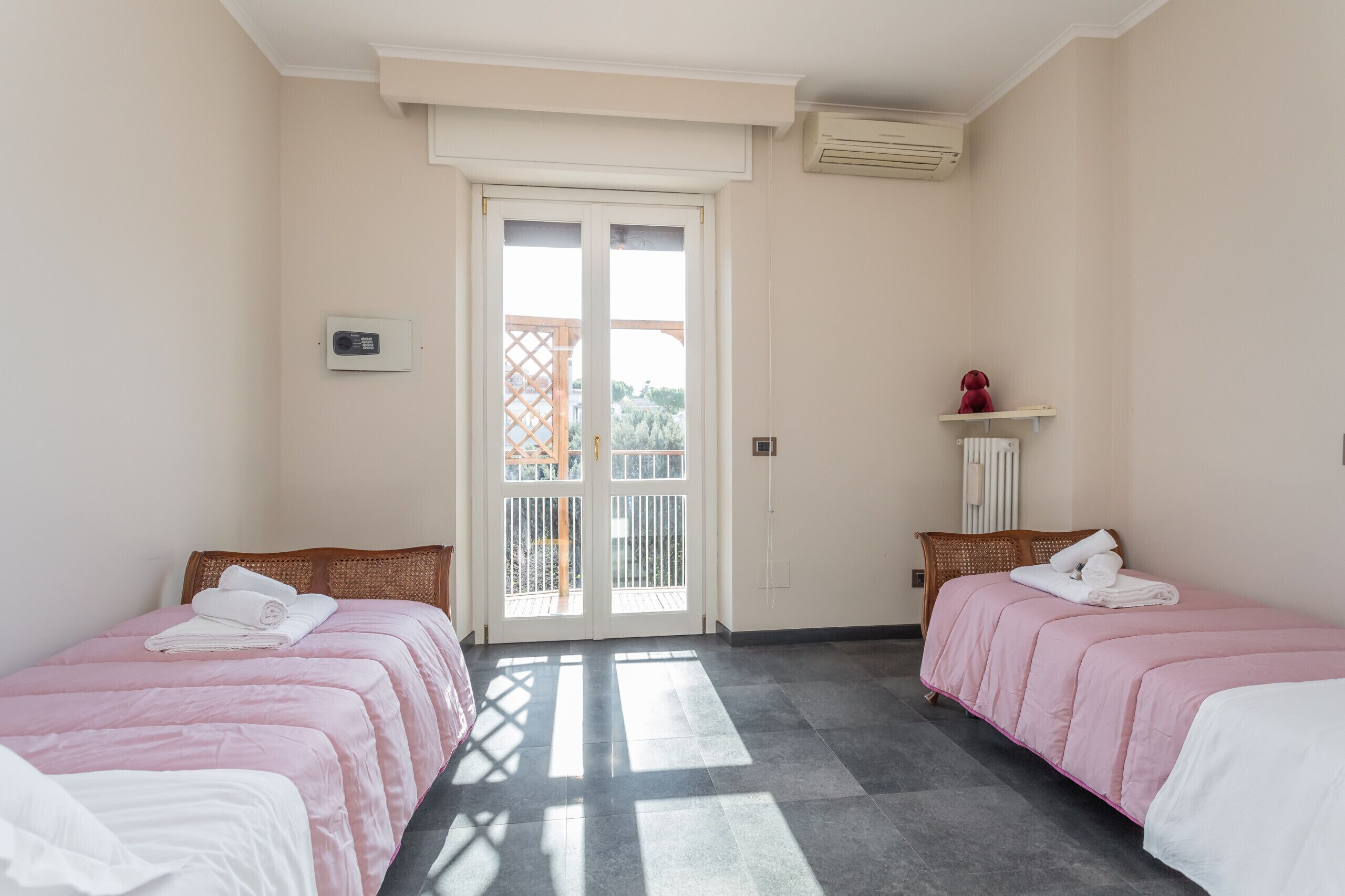 Habitación de hotel con dos camas, una puerta al balcón y un pequeño estante con un adorno.