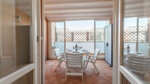 A balcony with a table and chairs, a sliding glass door, and a view of a fence and buildings. - Monteverde 2BDR  Penthouse (Roma)