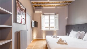 A hotel room with a large bed, a wooden floor, a radiator, a TV, and a window with open shutters. - Spanish Steps Rooftop Penthouse (Roma)