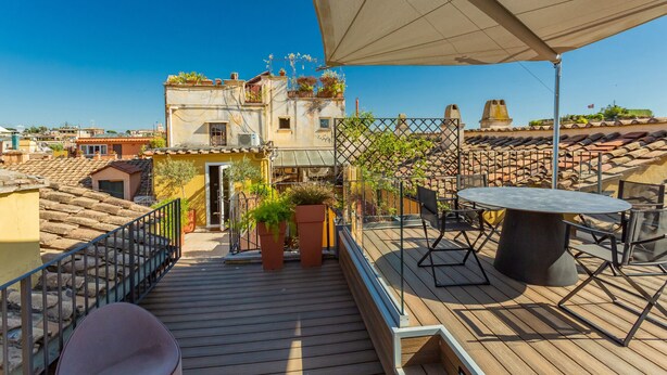 A rooftop terrace with a table and chairs, potted plants, and a view of surrounding buildings. - Spanish Steps Rooftop Penthouse (Roma)