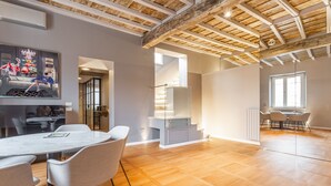 A spacious room with a wooden floor, a dining area with a table and chairs, a staircase, and a large window. - Spanish Steps Rooftop Penthouse (Roma)