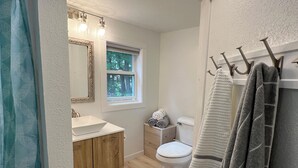 Un baño con tocador de madera, inodoro y ventana con vista a árboles.