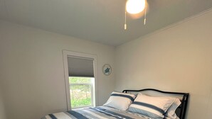Un dormitorio con cama, suelo de madera oscura, ventilador de techo y ventana con persianas.