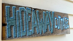 Un letrero de madera con el texto 'Hideaway Cottage' en letras azules.