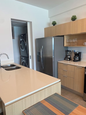 A modern kitchen with a stainless steel refrigerator, a built-in oven, a coffee maker, and a sink.