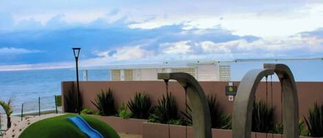 A beachside area with a playground, including a slide and swings, and a view of the ocean.