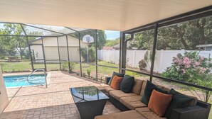 An outdoor patio with a sectional sofa, a glass coffee table, and a brick floor.