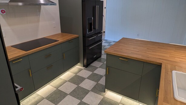 A compact kitchen with a black refrigerator, a stainless steel range hood, and a checkered tile floor.