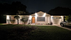 A modern two-story house with a garage, illuminated exterior lights, and a well-maintained lawn.
