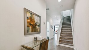 Ein moderner Flur mit einer Glas- und Holzkonsole, einer Treppe und einem gerahmten abstrakten Gemälde.