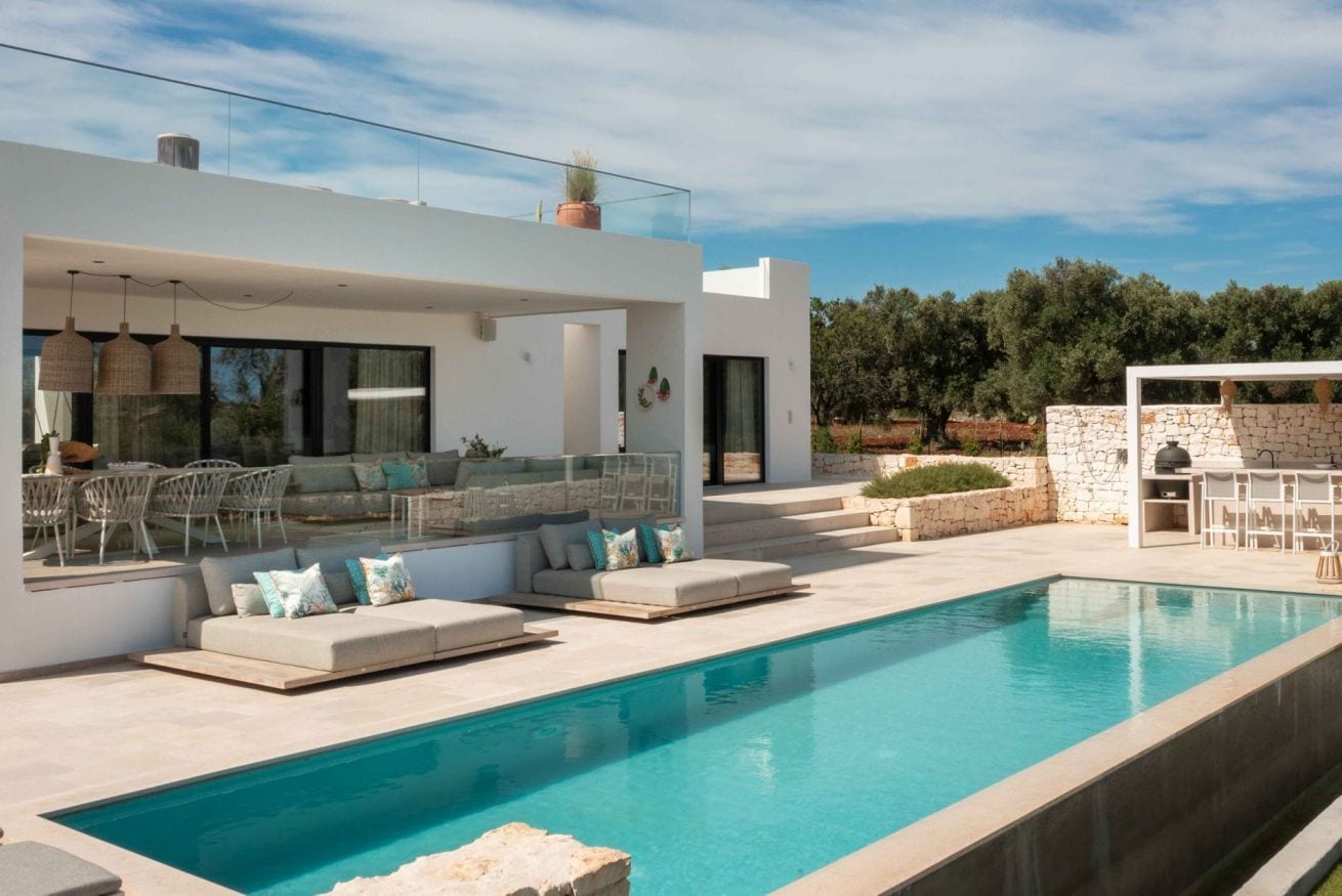 A modern house with a swimming pool, outdoor seating, and a stone wall.