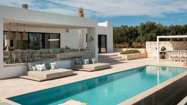Et moderne hus med swimmingpool, udendørs møbler og en stenvæg.