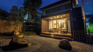 Ein modernes Haus mit hellem Innenraum, einer sichtbaren Treppe und einem Garten mit Steinen und einem Holzzaun.
