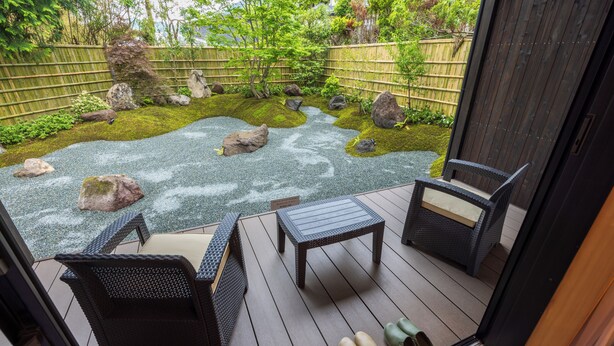 Eine Terrasse mit Korbmöbeln, einem kleinen Tisch und einem Paar Schuhe auf dem Boden.