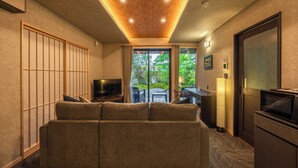 Ein modernes Hotelzimmer mit Sofa, Fernseher und Blick auf den Garten durch die Glastür.