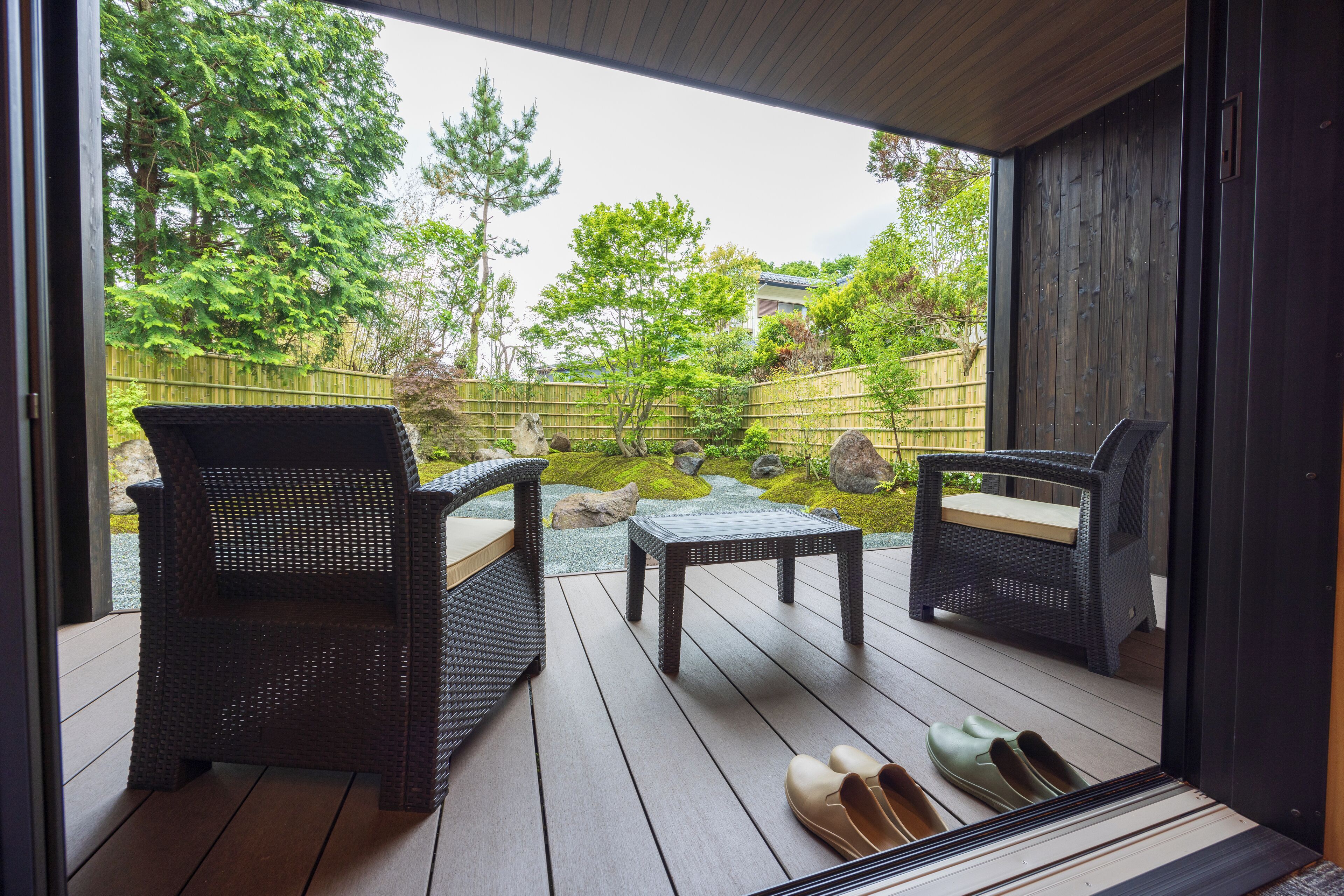 A wooden deck with wicker furniture and a small table, overlooking a garden with rocks and trees.