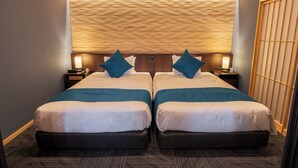Ein Hotelzimmer mit zwei Betten, einem hölzernen Kopfteil und einem traditionellen japanischen Shoji-Bildschirm.