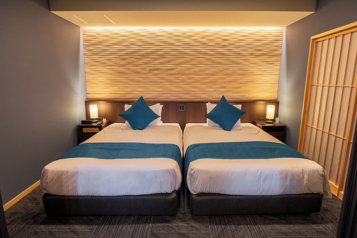 Habitación de hotel con dos camas, cabecero de madera y una tradicional pantalla japonesa shoji.