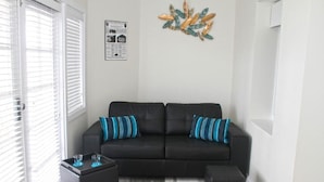 A living room with a black sofa, two striped pillows, a small black side table with two glasses, and a decorative wall piece.