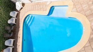 A rectangular swimming pool with a curved edge, surrounded by a tiled patio.