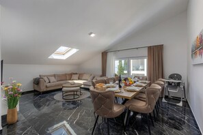 Ein modernes Wohnzimmer mit einer Couch, einem Esstisch, Stühlen, einem Oberlicht und einem fensterbelaubten Fenster.