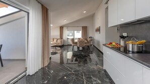 Uma cozinha moderna com piso de mármore, uma sala de jantar com mesa e cadeiras, e uma sala de estar com sofá e mesinha de centro.