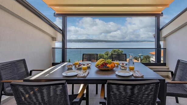 Mesa de jantar com itens de café da manhã, cadeiras de vime e vista para o mar.