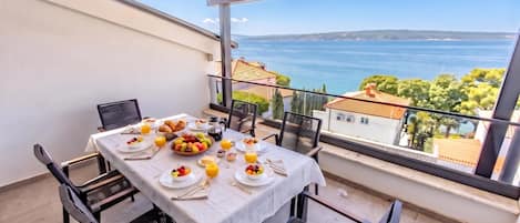 A balcony with a table set for breakfast, overlooking a coastal view.