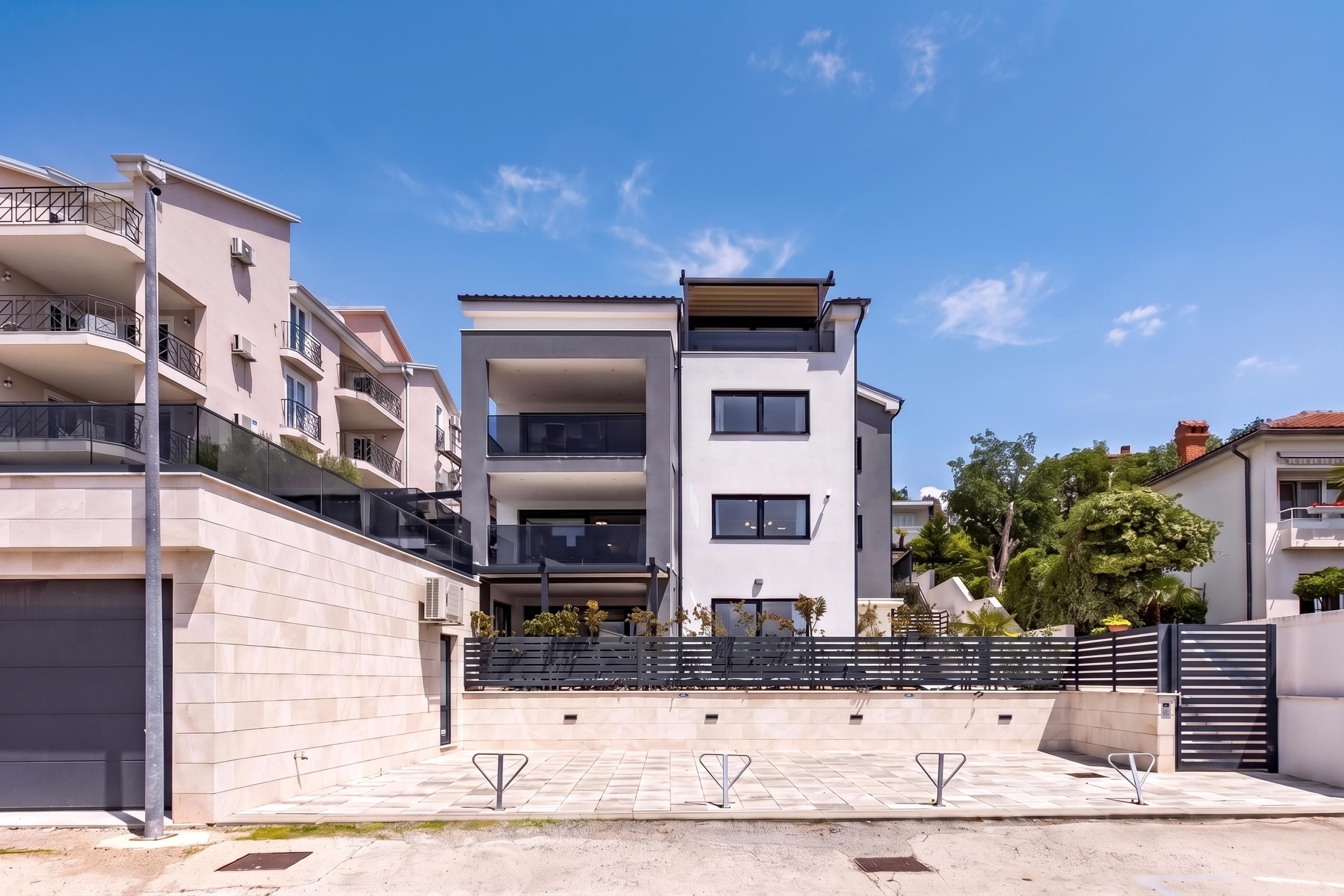 A modern multi-story residential building with balconies, a gated entrance, and a paved driveway.
