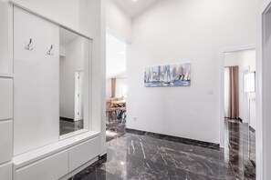 A modern interior with a hallway leading to a dining area, a large mirror, and a painting on the wall.