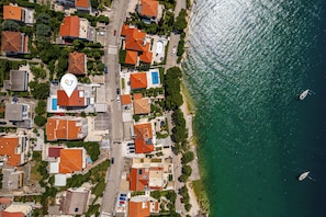 Vue aérienne d’une zone résidentielle côtière, avec des maisons, une route et une étendue d’eau où se trouvent des bateaux.